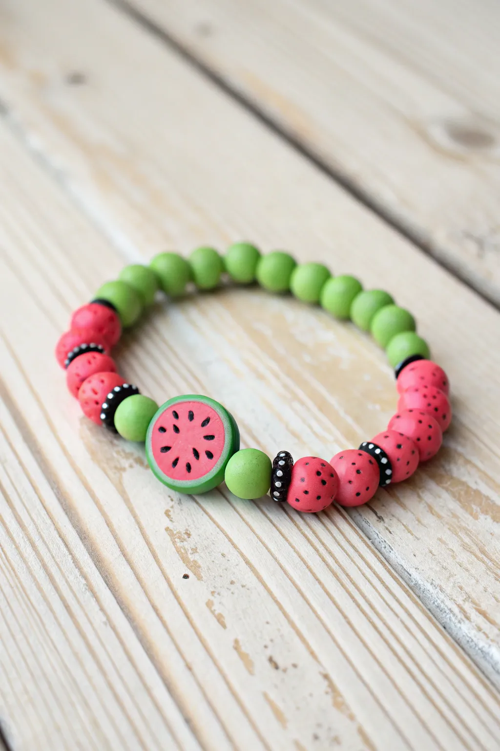 Watermelon-inspired clay bead bracelet in green, pink, and seed-like black accents on light wood