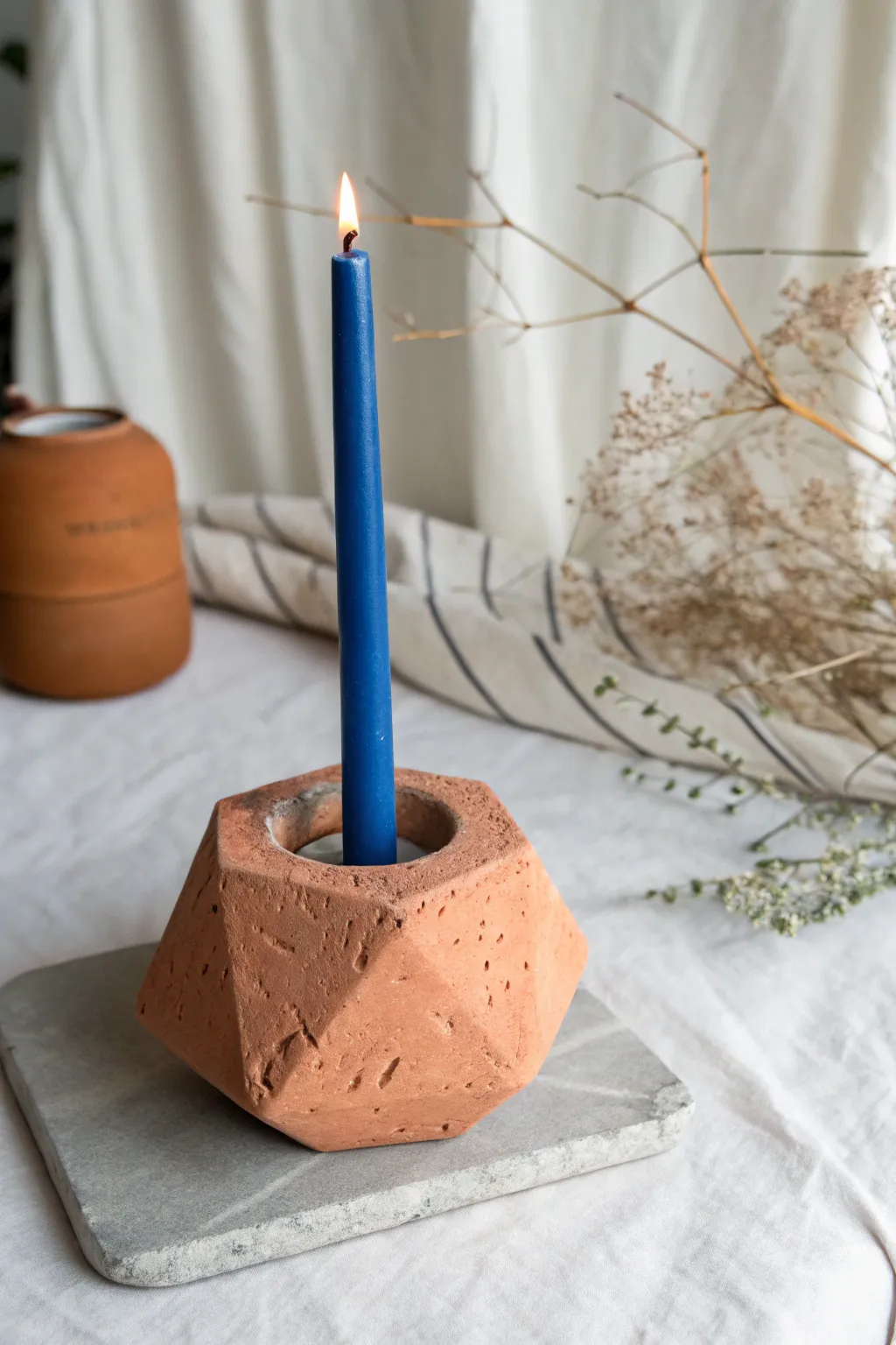 Chunky air-dry clay candle holder in terracotta with a slim cobalt candle and cozy warm glow.