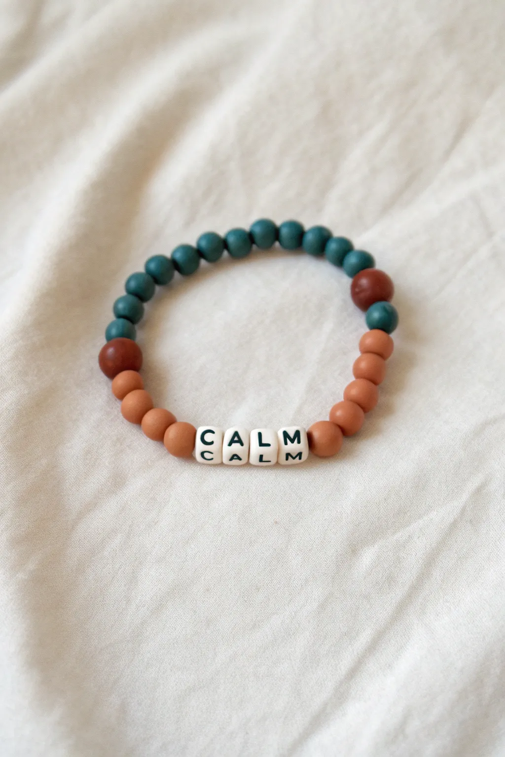 Minimal mantra bracelet with clay heishi beads in terracotta and teal for calm, bold contrast.