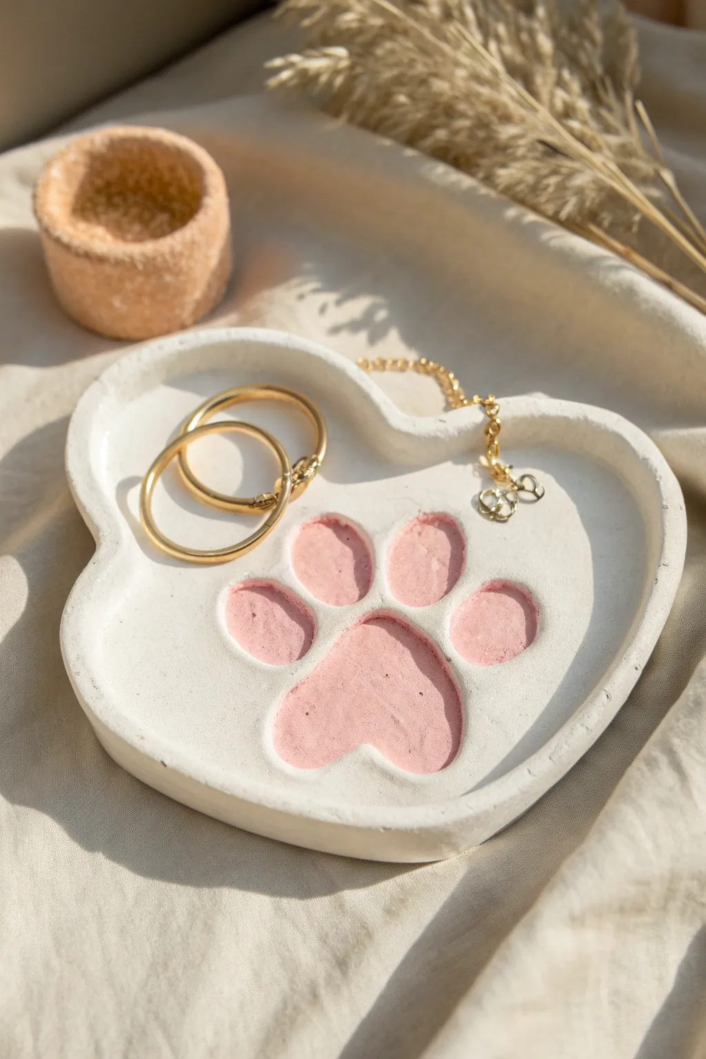 Kawaii cat paw air dry clay tray in blush and white, holding dainty earrings and a bracelet
