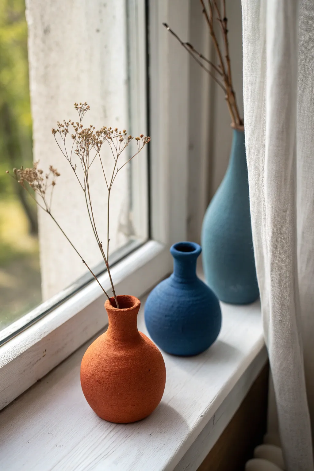 Mini clay bud vase buddies in bold tones, glowing in soft window light with tiny dried stems
