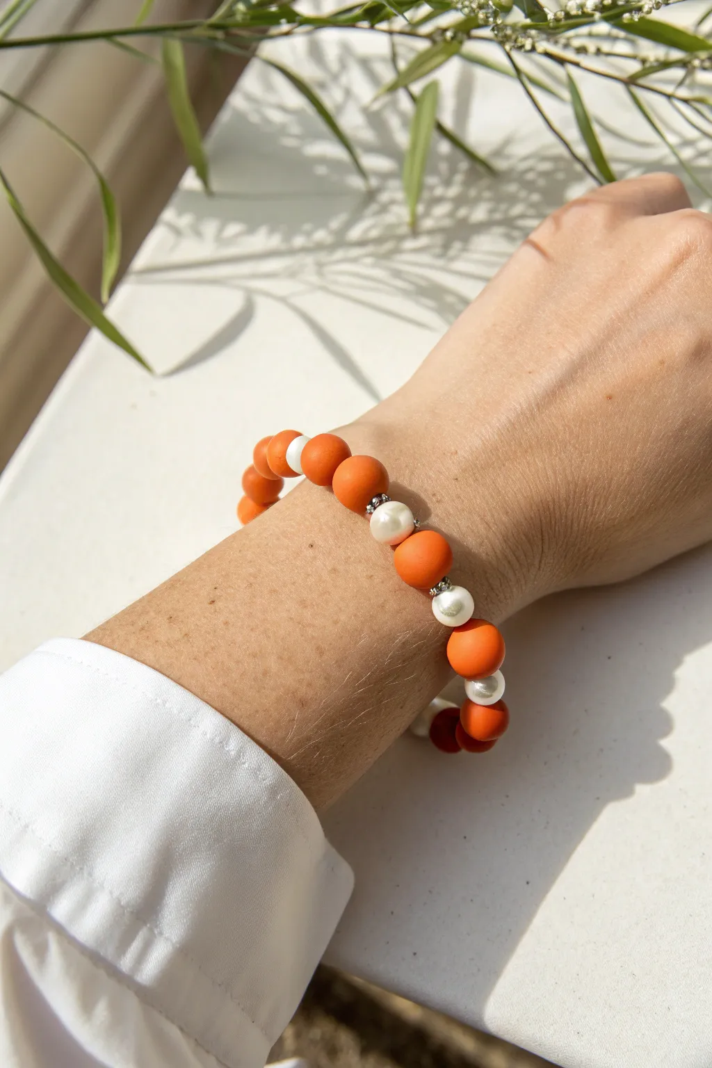 Bold orange clay beads with delicate pearl accents for a minimalist bracelet look.