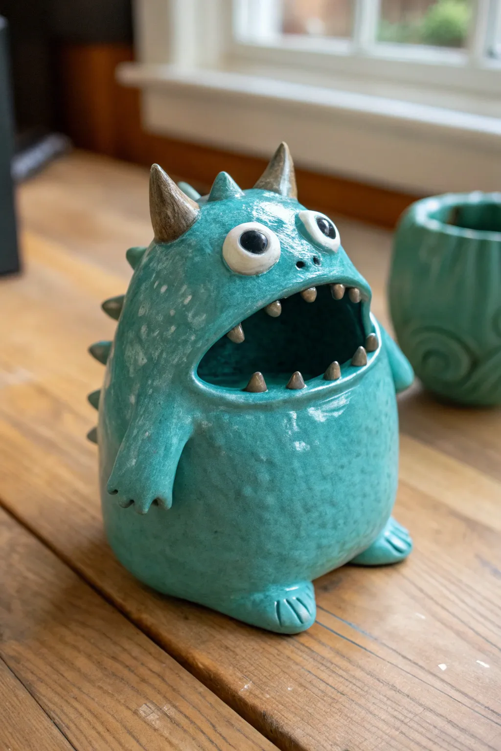 Teal spiky pinch pot monster with a stubby tail, bold color and clean minimalist charm.