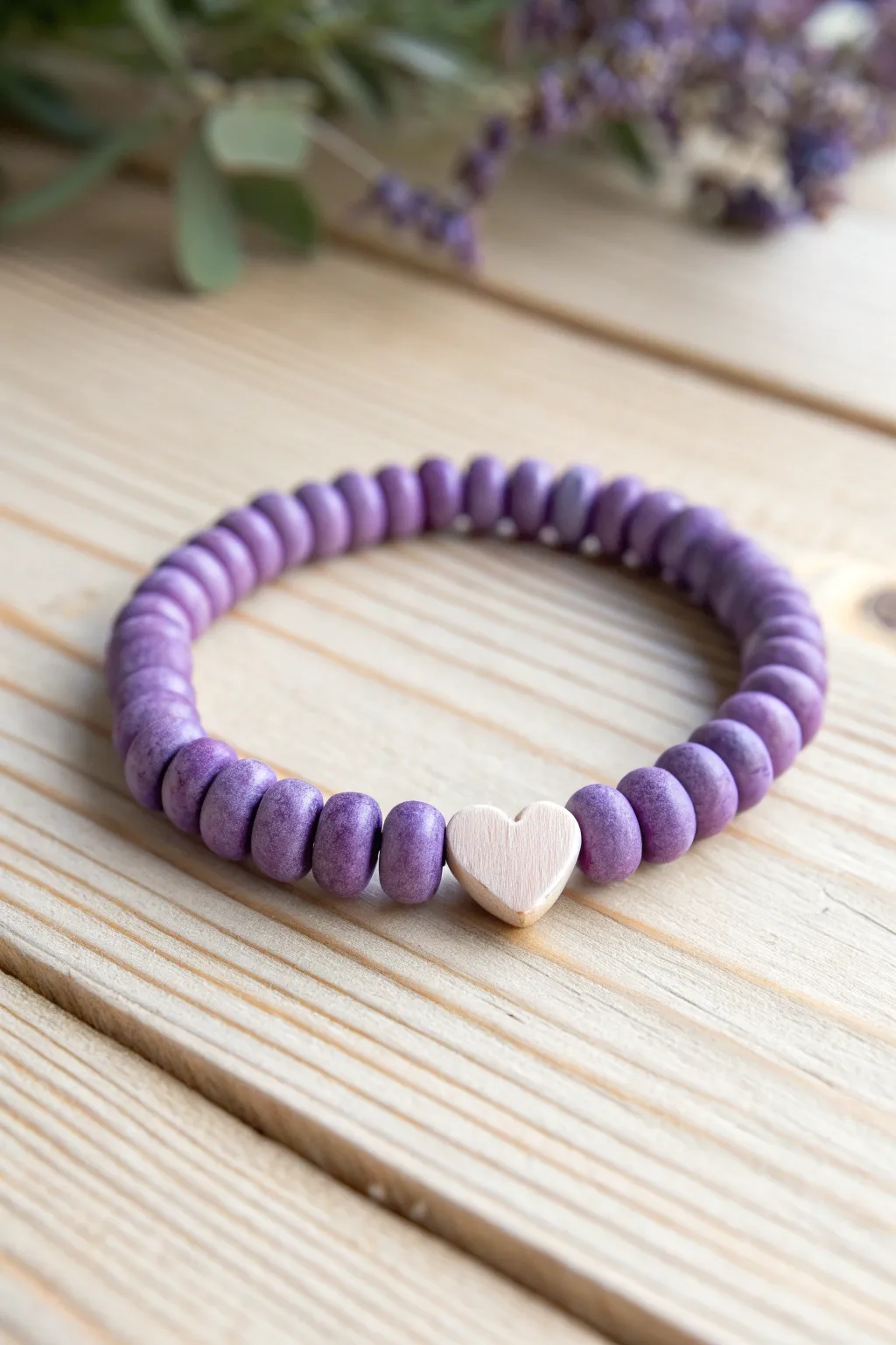 Purple heishi bracelet with a lilac heart centerpiece, styled minimal on pale wood