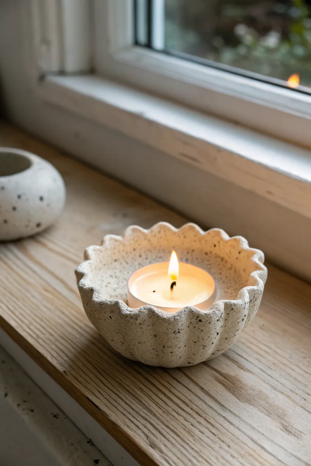 Scalloped clay tea light holder glowing softly, minimal Nordic style with a warm boho touch.