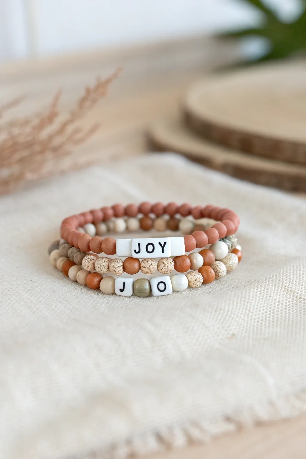 Stackable clay heishi bracelets with a JOY letter centerpiece in soft Scandinavian boho neutrals.