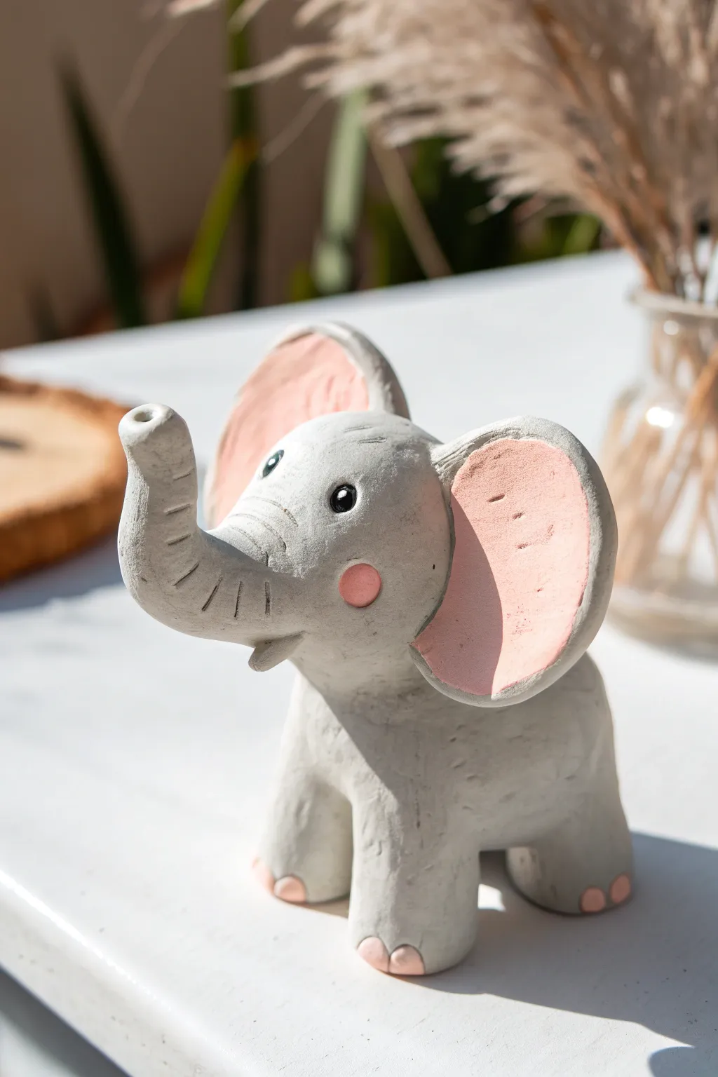 Cute air dry clay elephant with oversized ears, matte gray and pink on a soft peach backdrop