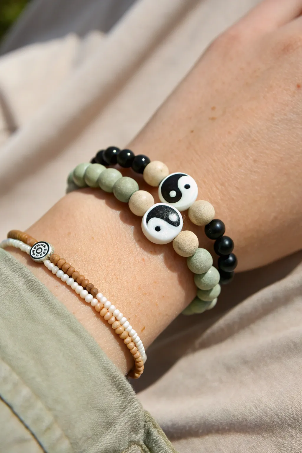 Stacked clay bead bracelets with a bold yin-yang centerpiece in minimalist black, white, and sage.