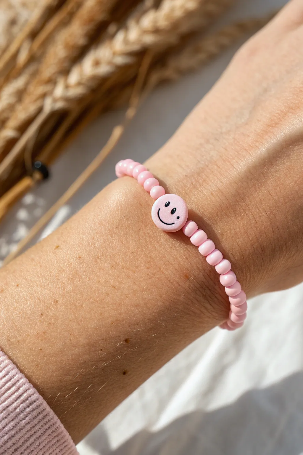 Pink heishi bracelet with an off-center smiley accent, styled minimal for a soft boho vibe.