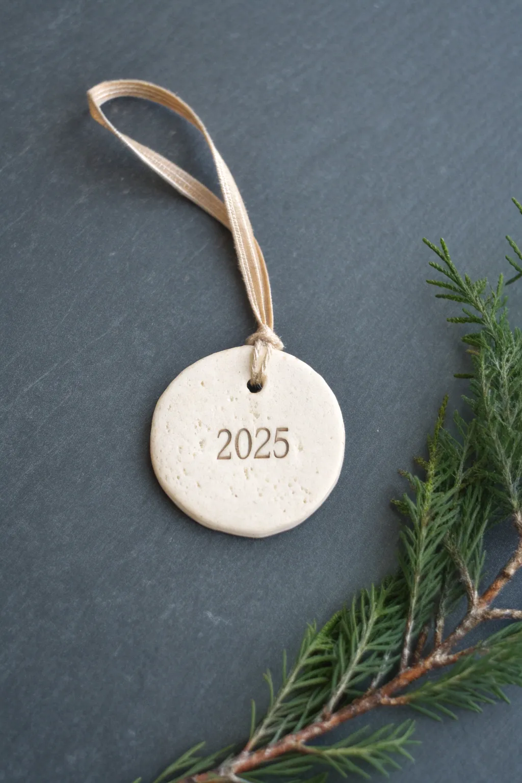 Minimalist year-stamped clay ornament keepsake, styled with evergreen for a cozy Nordic look