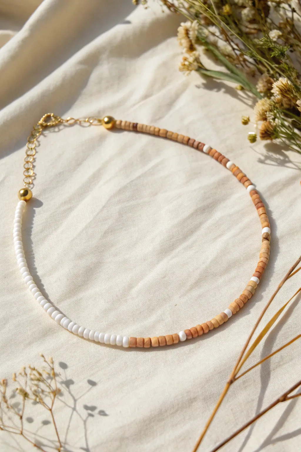 Minimal heishi choker in creamy neutrals with a terracotta accent, clean Scandinavian styling.
