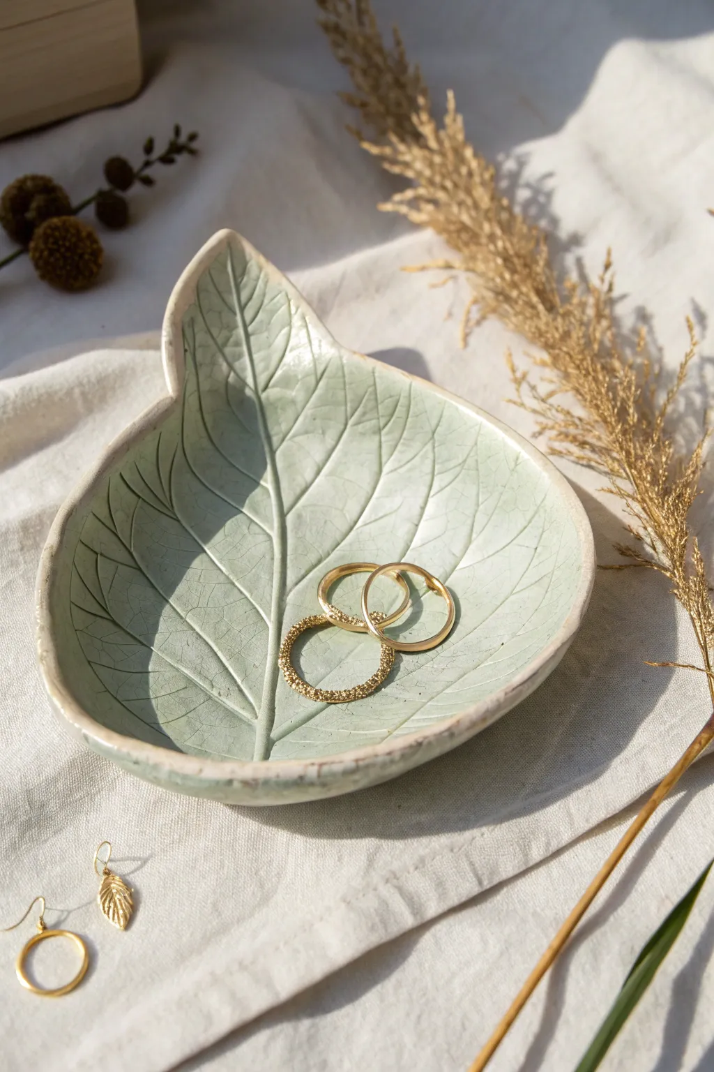 Leaf-imprint clay jewelry dish with soft sage wash, styled with earrings and stacked rings.