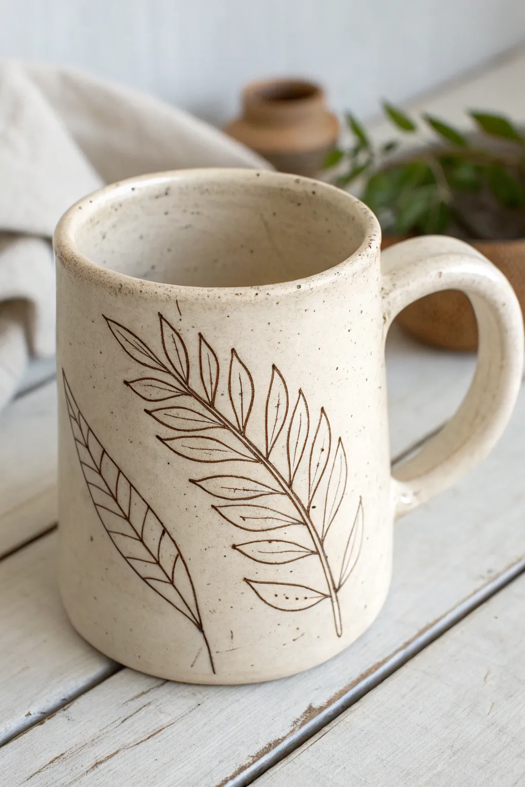 Sgraffito slab mug with simple leafy line art, minimalist Scandinavian mood with soft boho warmth.