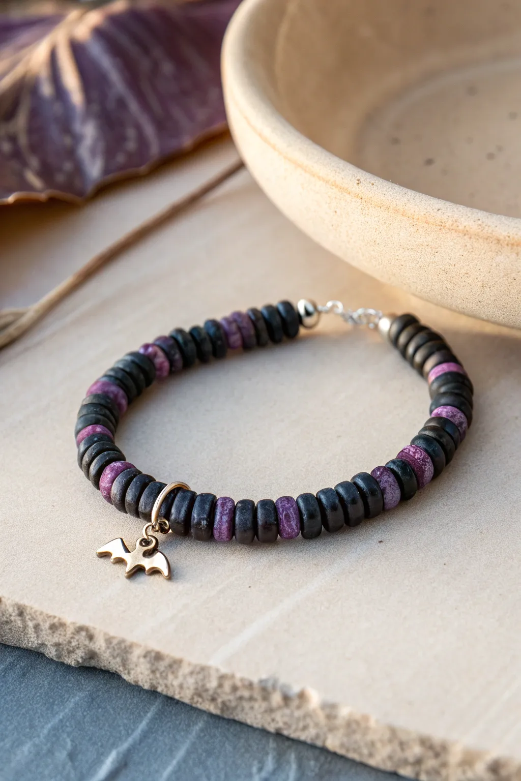 Moody midnight heishi bracelet with a tiny bat charm, minimalist Halloween look in deep purple.