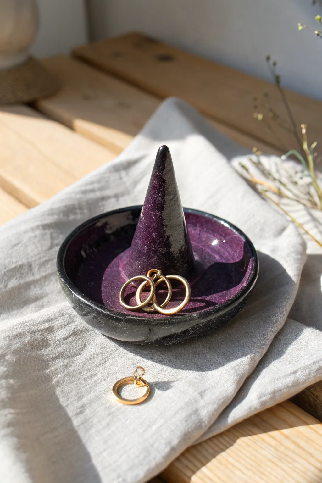 A minimalist witch hat ring dish in black and deep purple glaze, styled with simple gold jewelry.