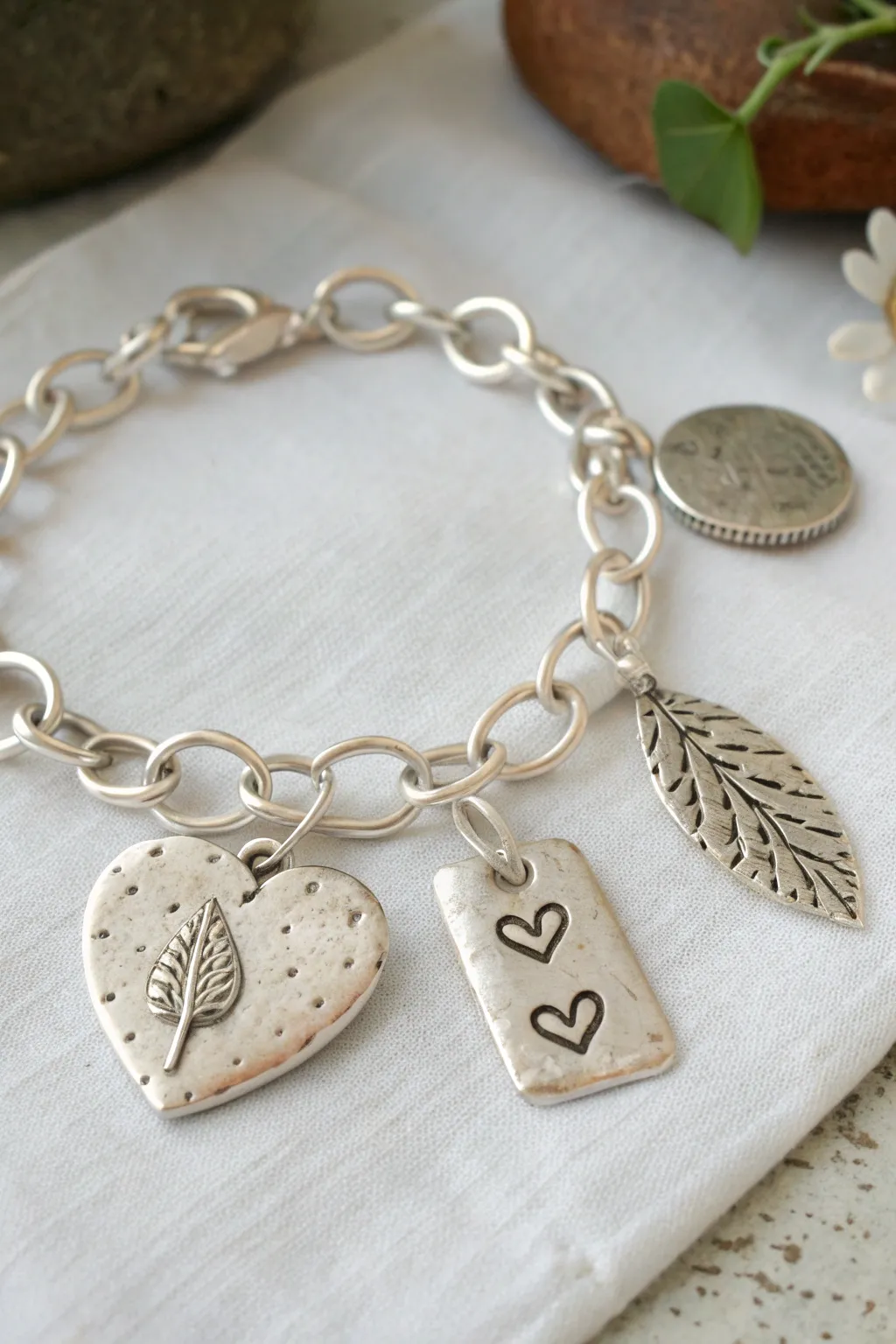 Metal clay charm bracelet mix with heart, tag and leaf charms, styled in soft minimalist tones.