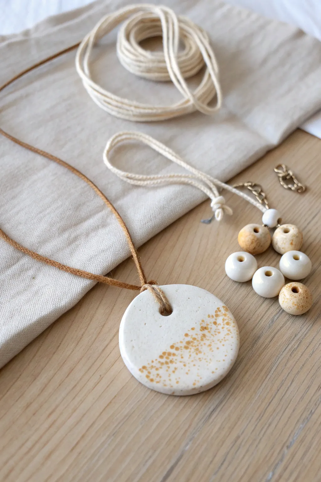 Tiny speckled clay pendant discs and beads, styled simply with linen cord for easy layering.