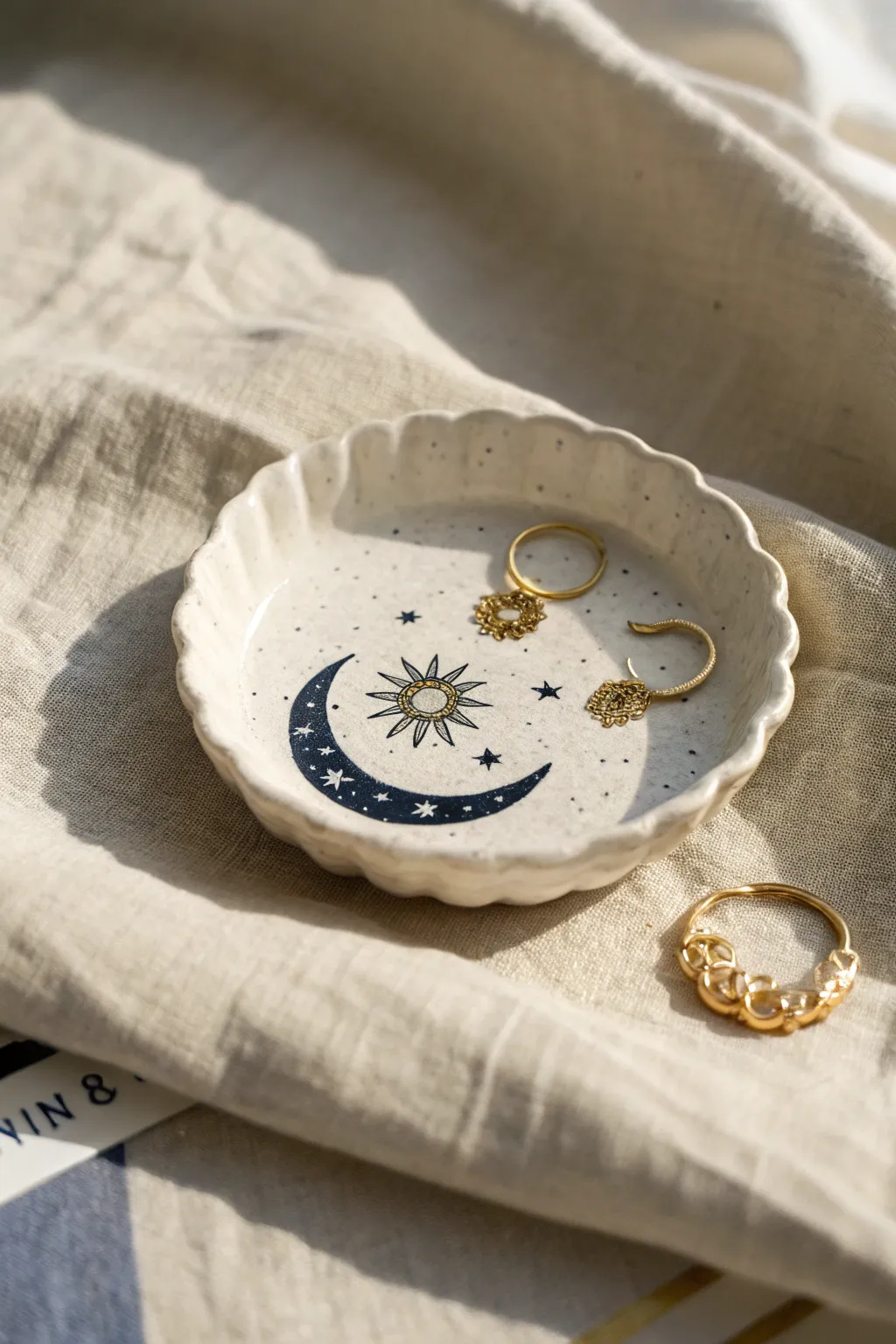 Minimal porcelain jewelry plate with moon and sun motif in navy and gold, softly styled.