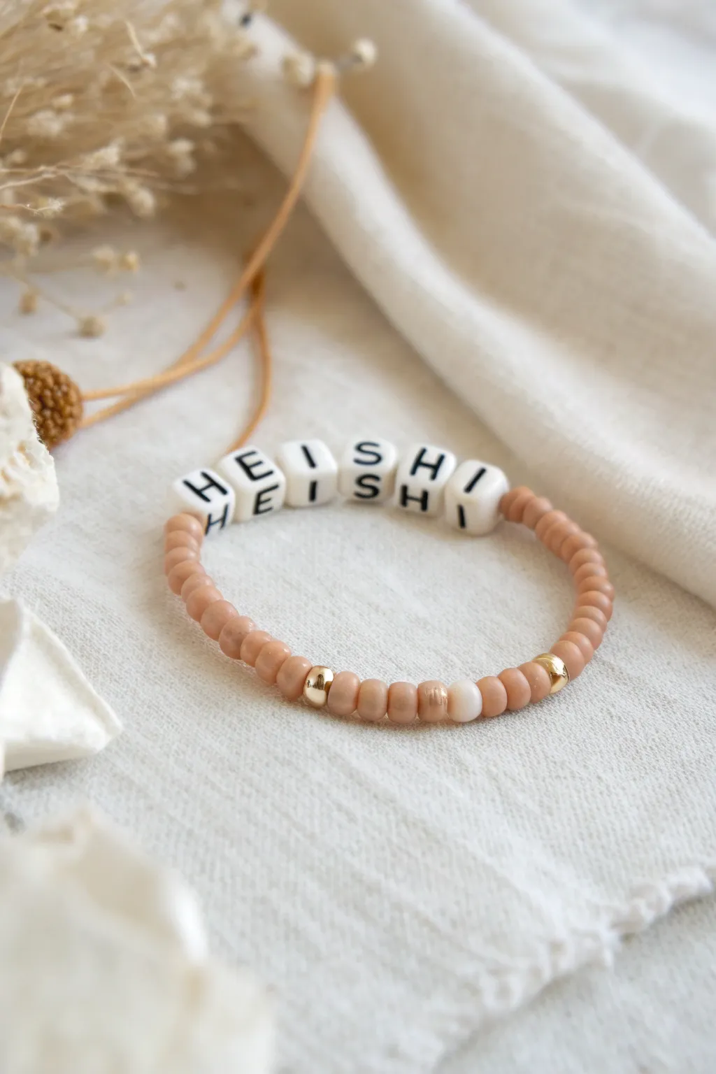 Warm neutral clay heishi name bracelet on linen, minimalist boho style with cozy handmade charm.