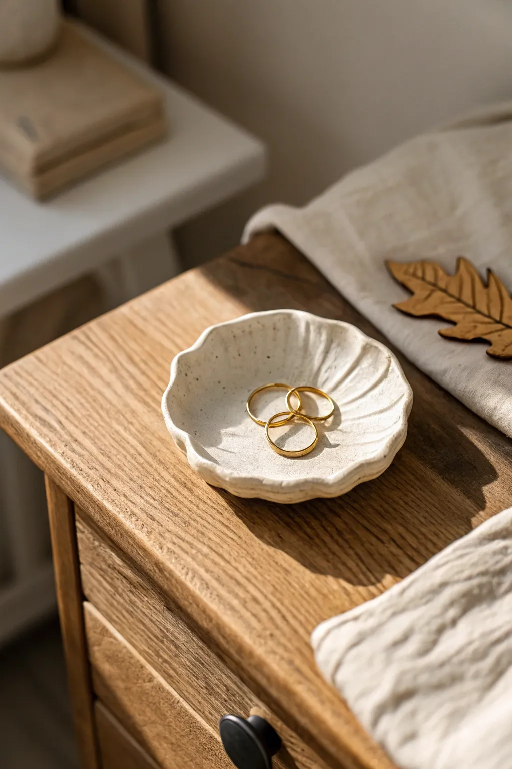Minimal handmade clay trinket dish holding rings, warmly lit on an airy Scandinavian nightstand.