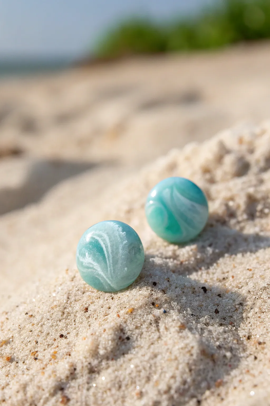 Translucent ocean-foam studs with soft white swirls, glowing gently on a sandy backdrop.