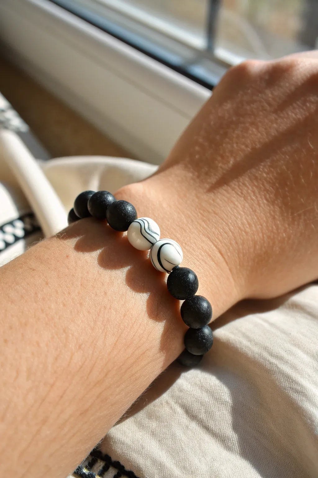 Minimal black and white clay bead bracelet with marbled swirl accents, softly lit.