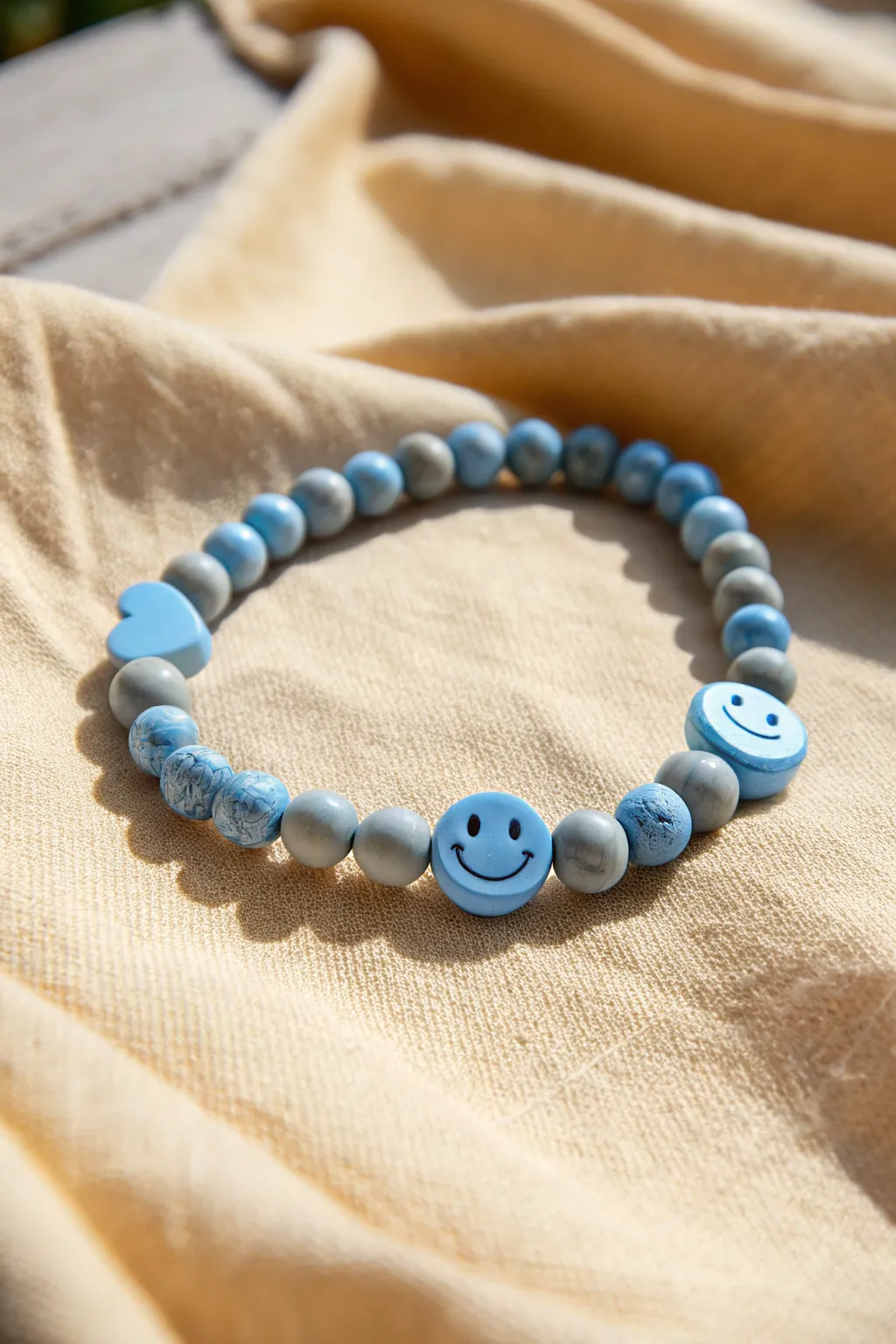 Baby blue clay bead bracelet with one smiley bead and one heart accent, playful and minimal.