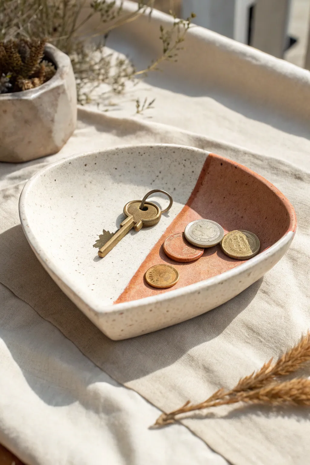 Two-tone rounded triangle clay catchall dish, folded corners, styled with coins and a key.