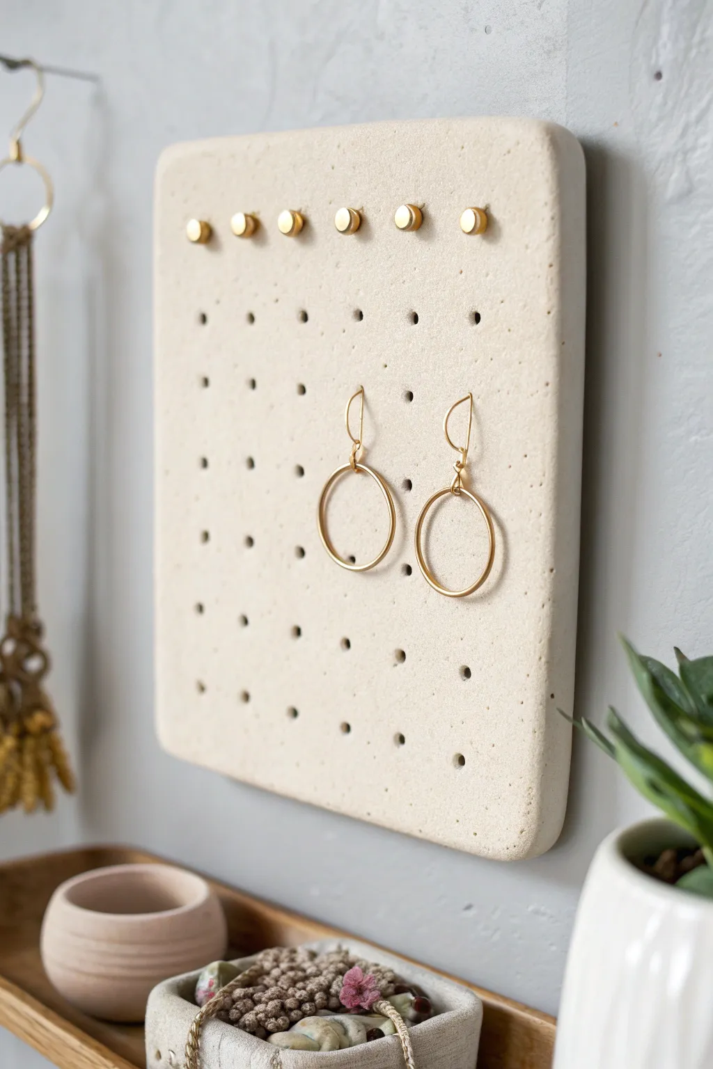 Minimal clay wall tile with peg holes, holding earrings neatly in a calm Scandinavian style