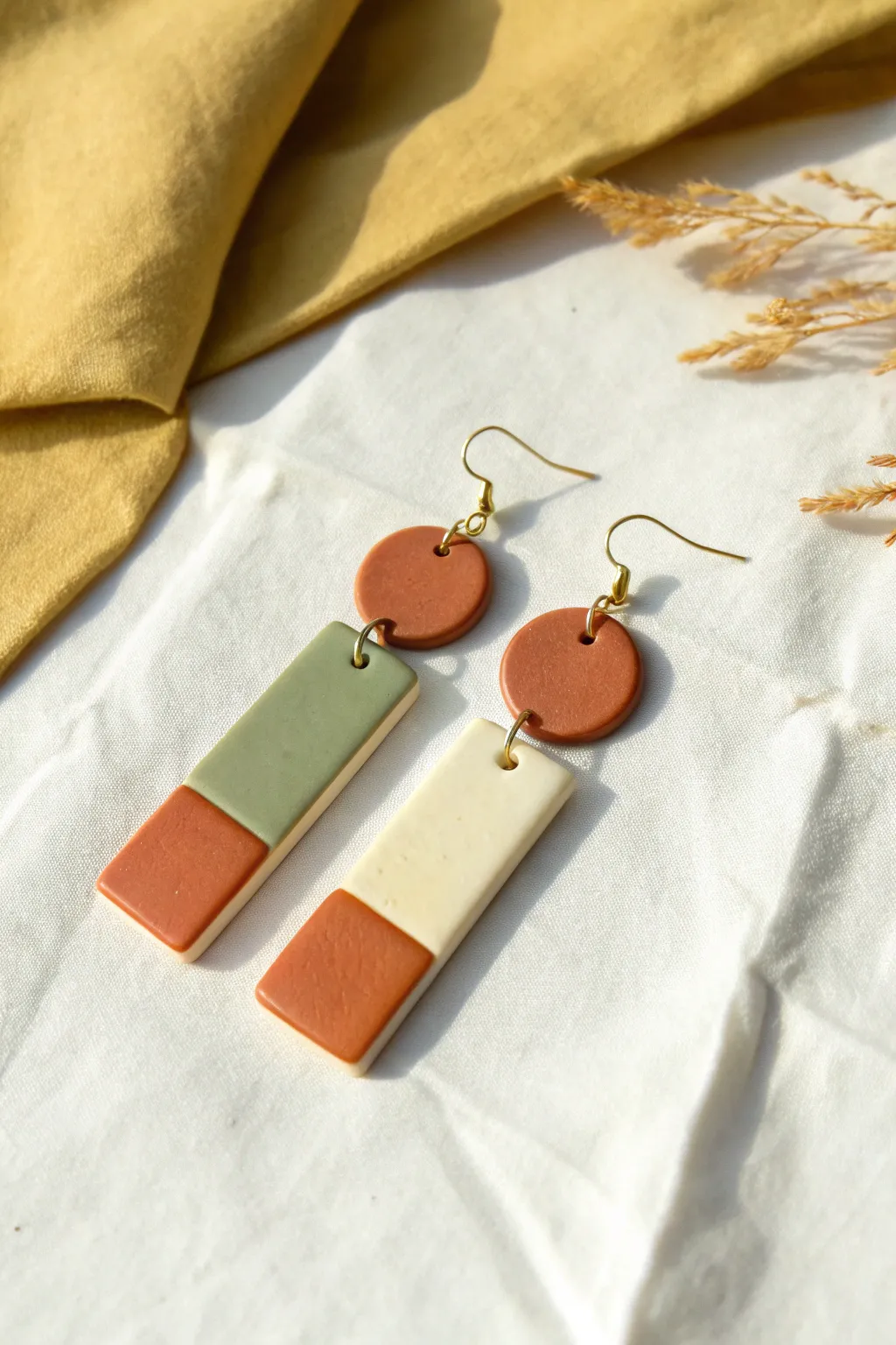 Simple color-block clay geometrics: circle and rectangle dangles in terracotta, sage, ivory.