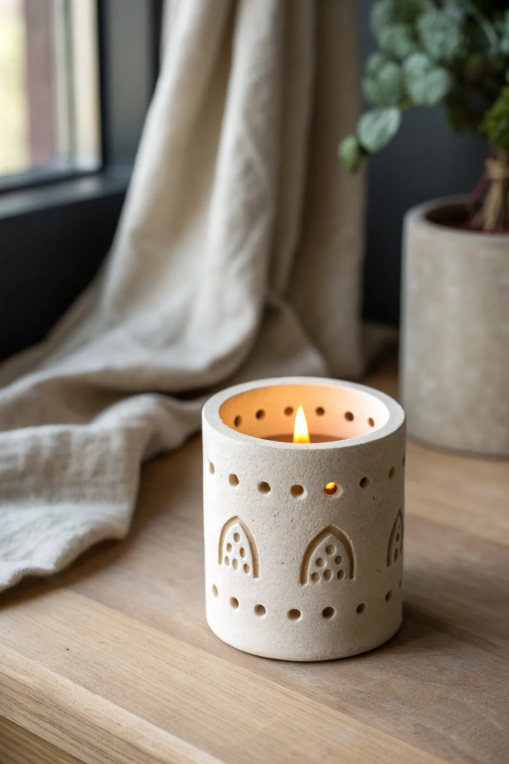 Minimal clay tea light holder with simple cutouts, glowing warmly in a cozy Scandinavian nook