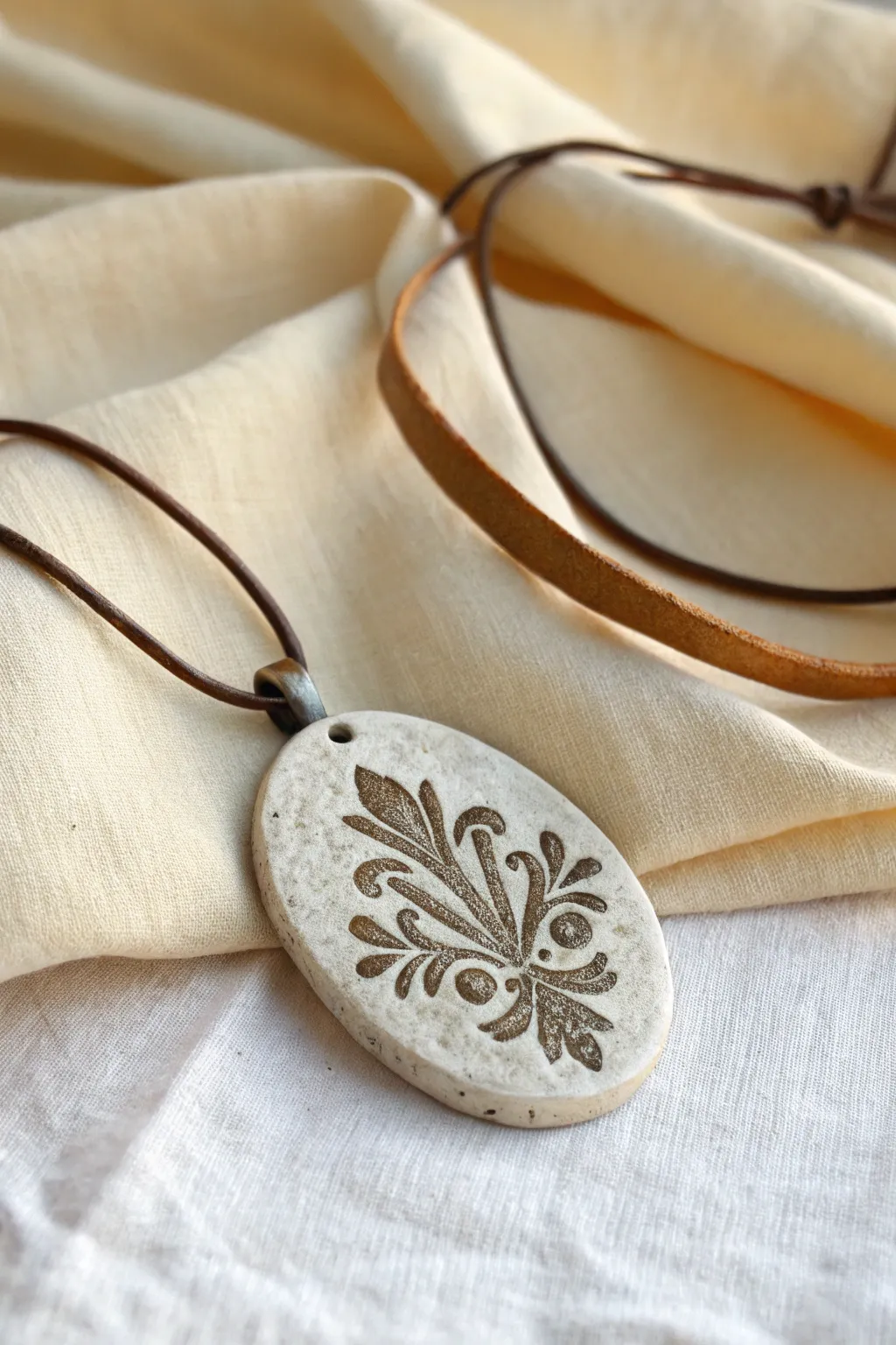 Oval clay medallion with a dark antiqued wash, highlighting deep stamped texture and handmade charm.