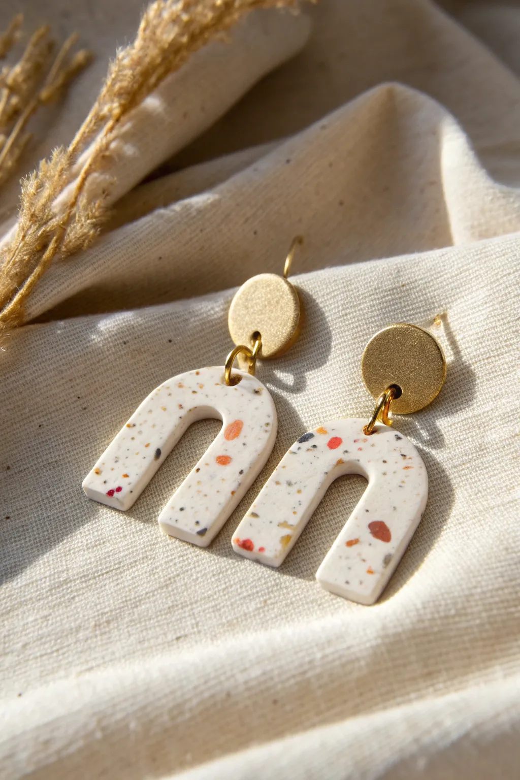 Minimalist arch polymer clay earrings with terrazzo speckles on linen, softly lit and bold.