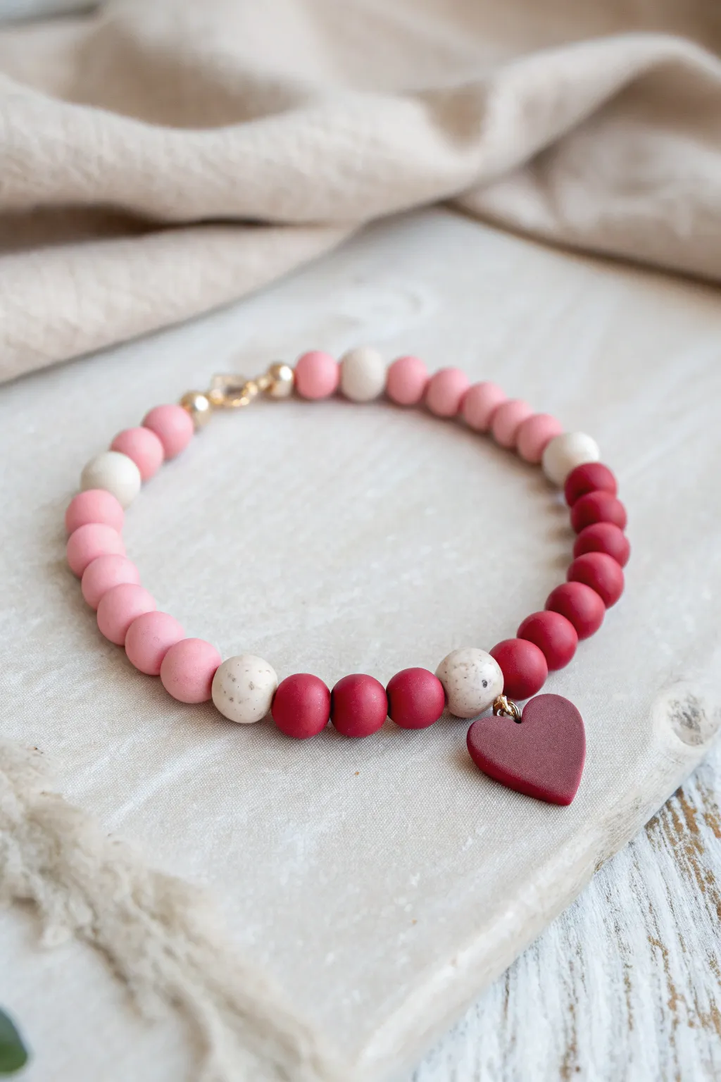 Split-half pink and red clay bead bracelet with a centered heart bead for sweet symmetry