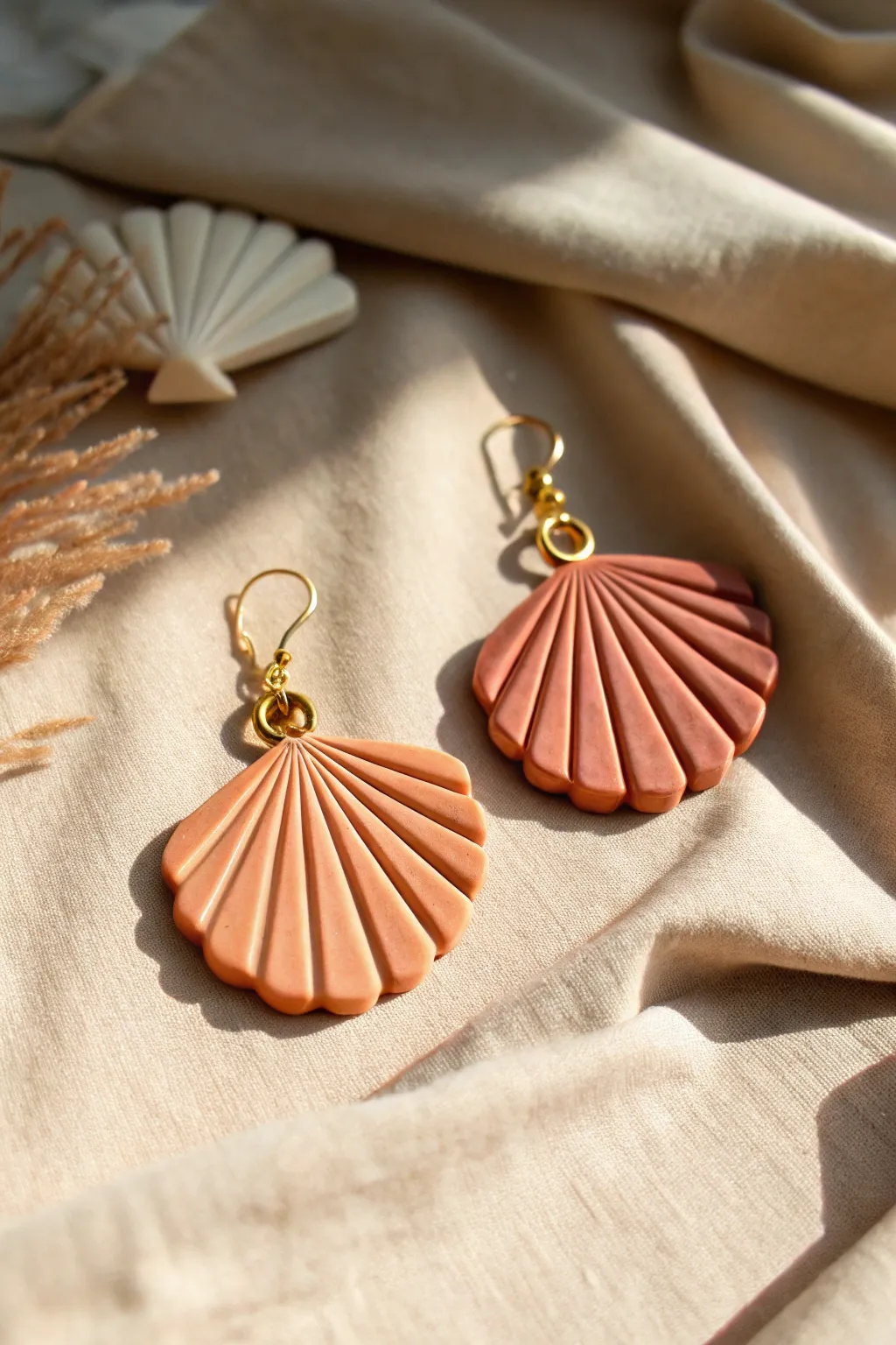 Scalloped fan clay earrings in warm sunset tones, minimalist boho styling on neutral linen
