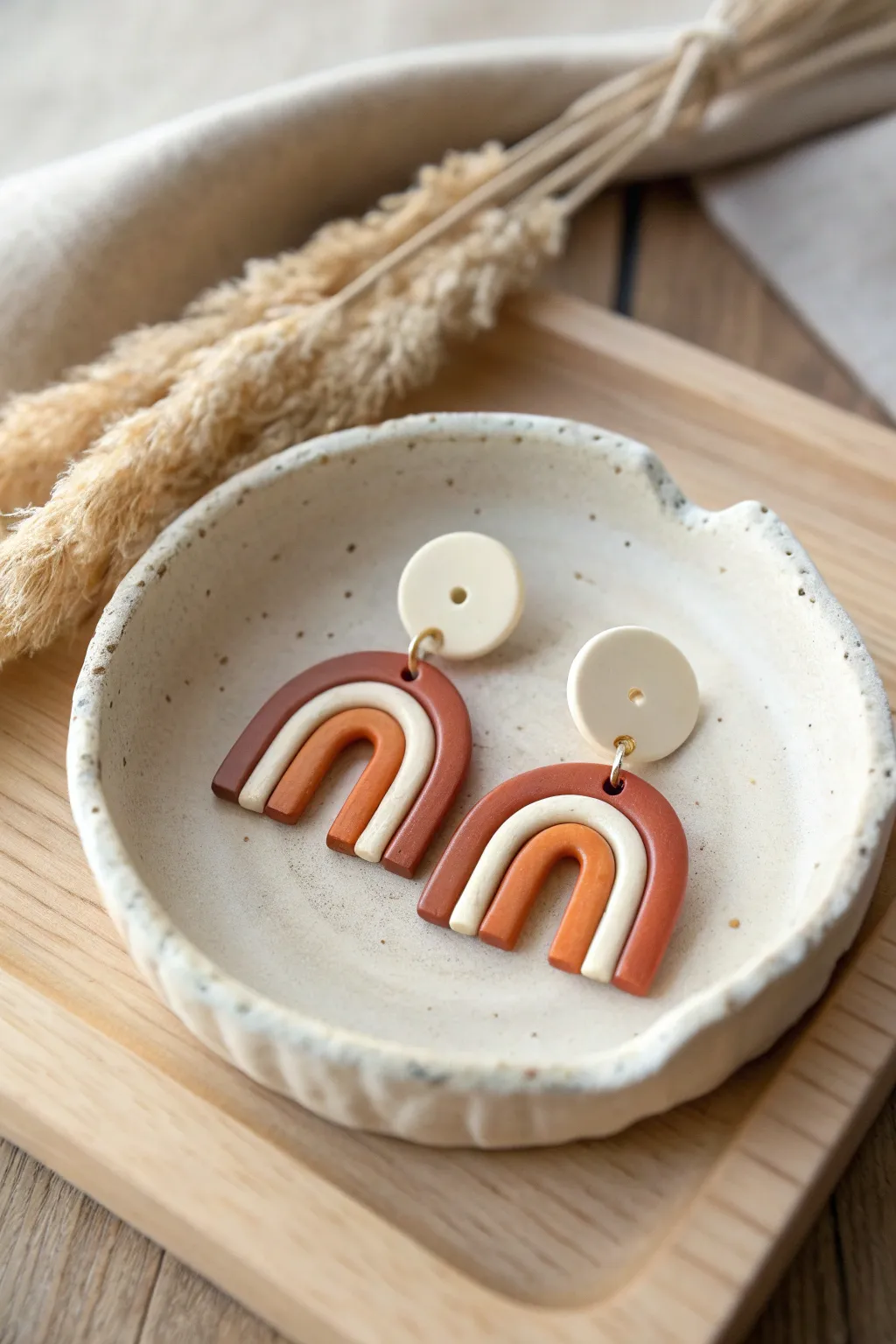 Minimal two-tone polymer clay arch earrings styled on a ceramic dish in soft natural light
