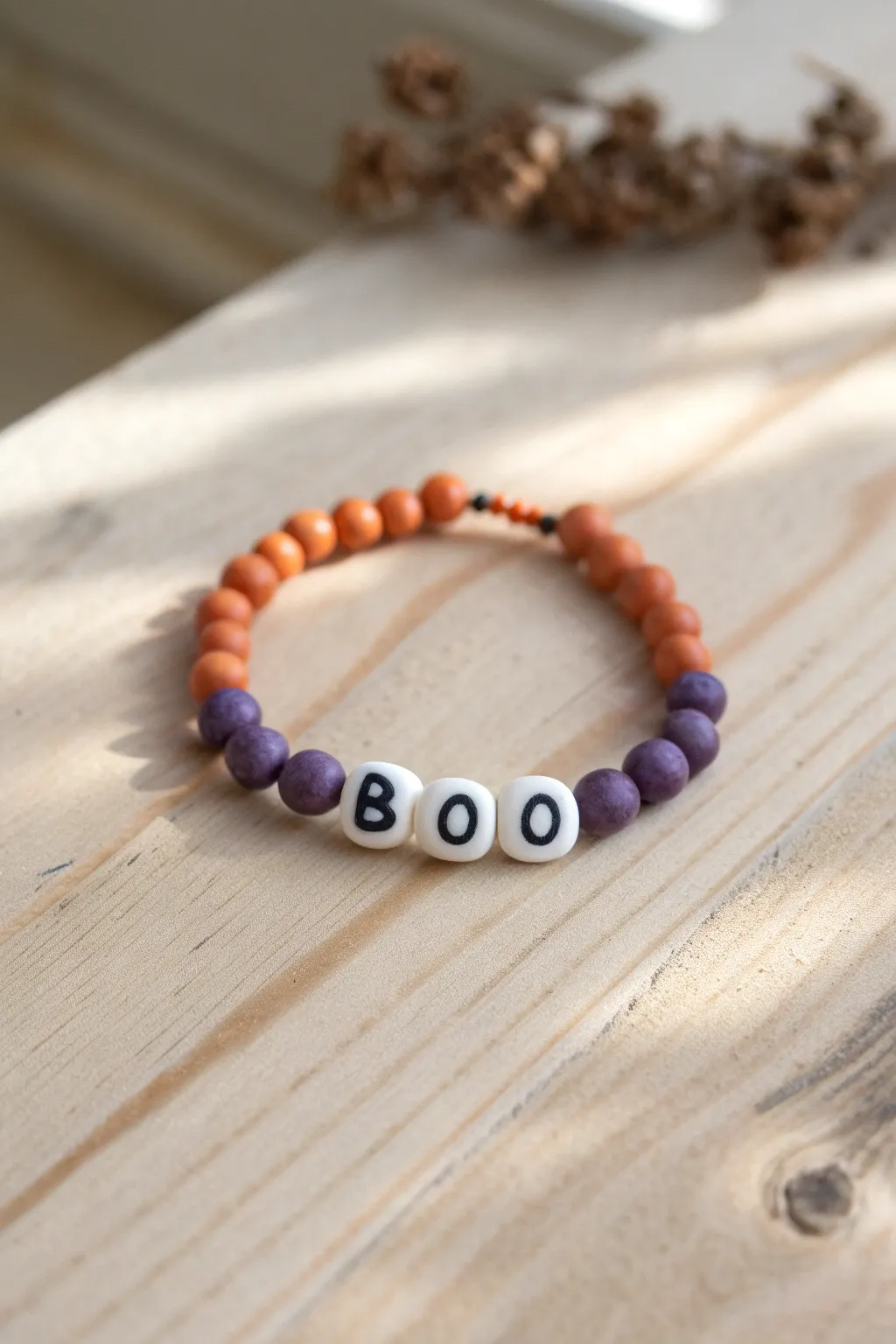 Minimal BOO bracelet with spooky orange and purple heishi spacers on pale wood background