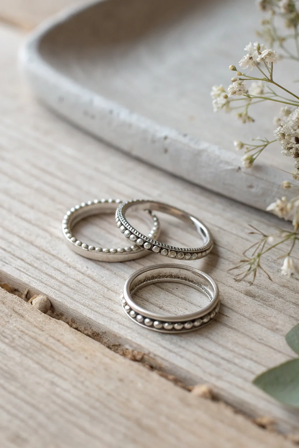 Minimal metal clay stacking rings with delicate syringe-dot borders, styled on pale wood.