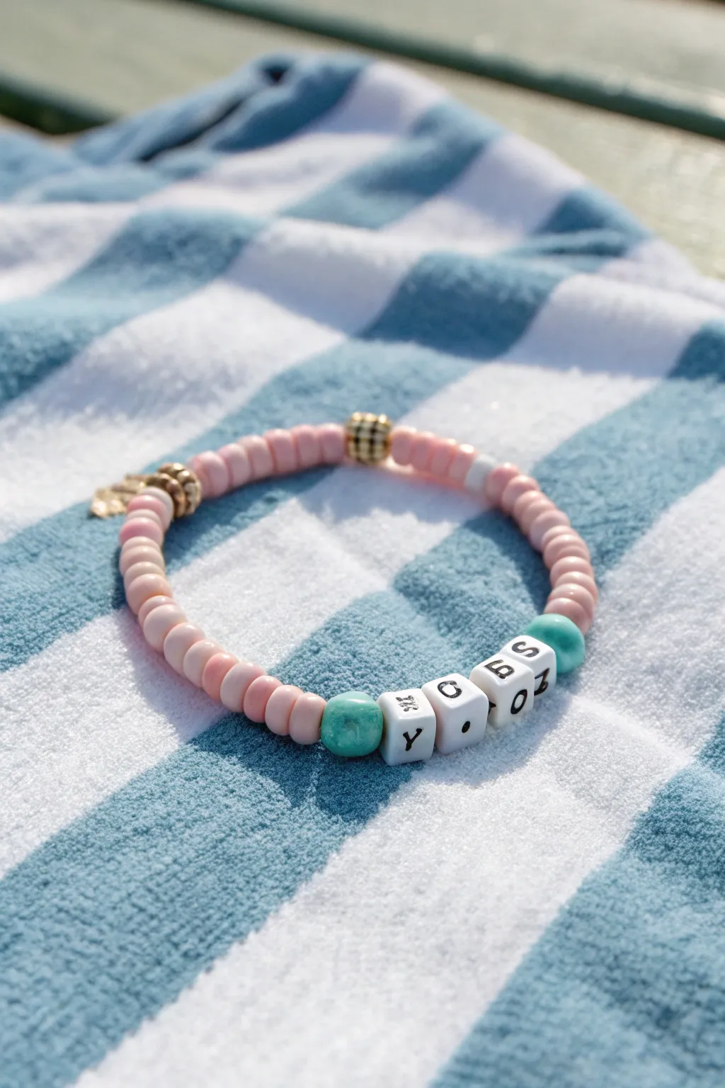 Preppy beach bracelet with pink and aqua color blocks on a crisp striped towel, minimal and chic.