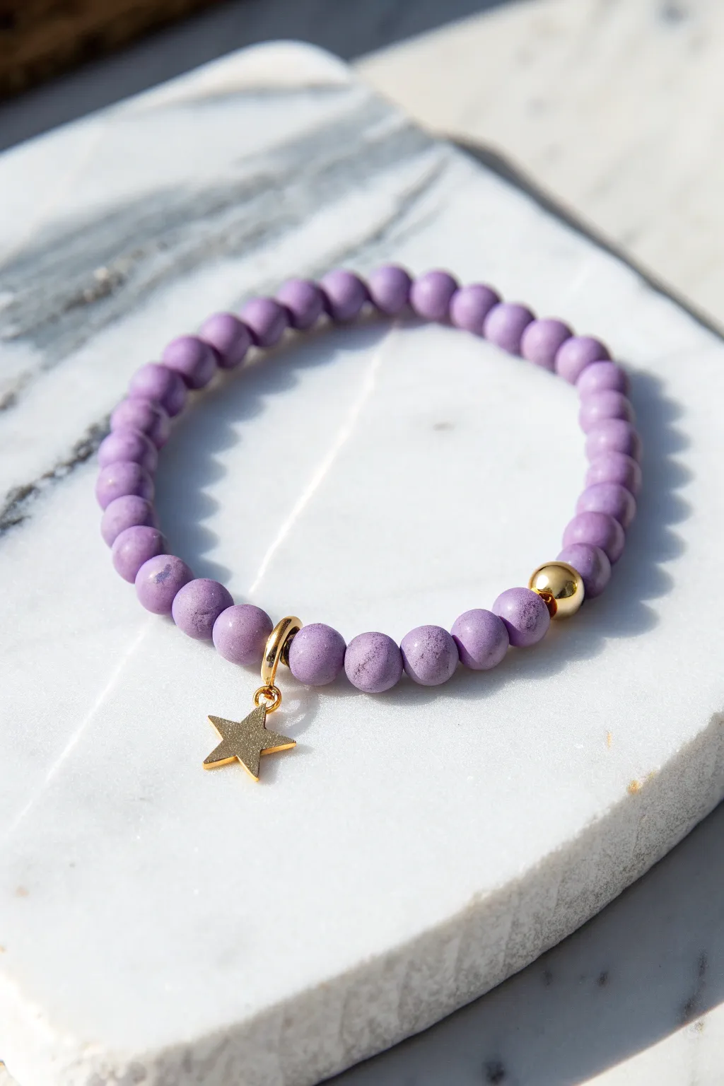 Lavender clay bead bracelet with a dangling star charm, minimalist and celestial on marble.