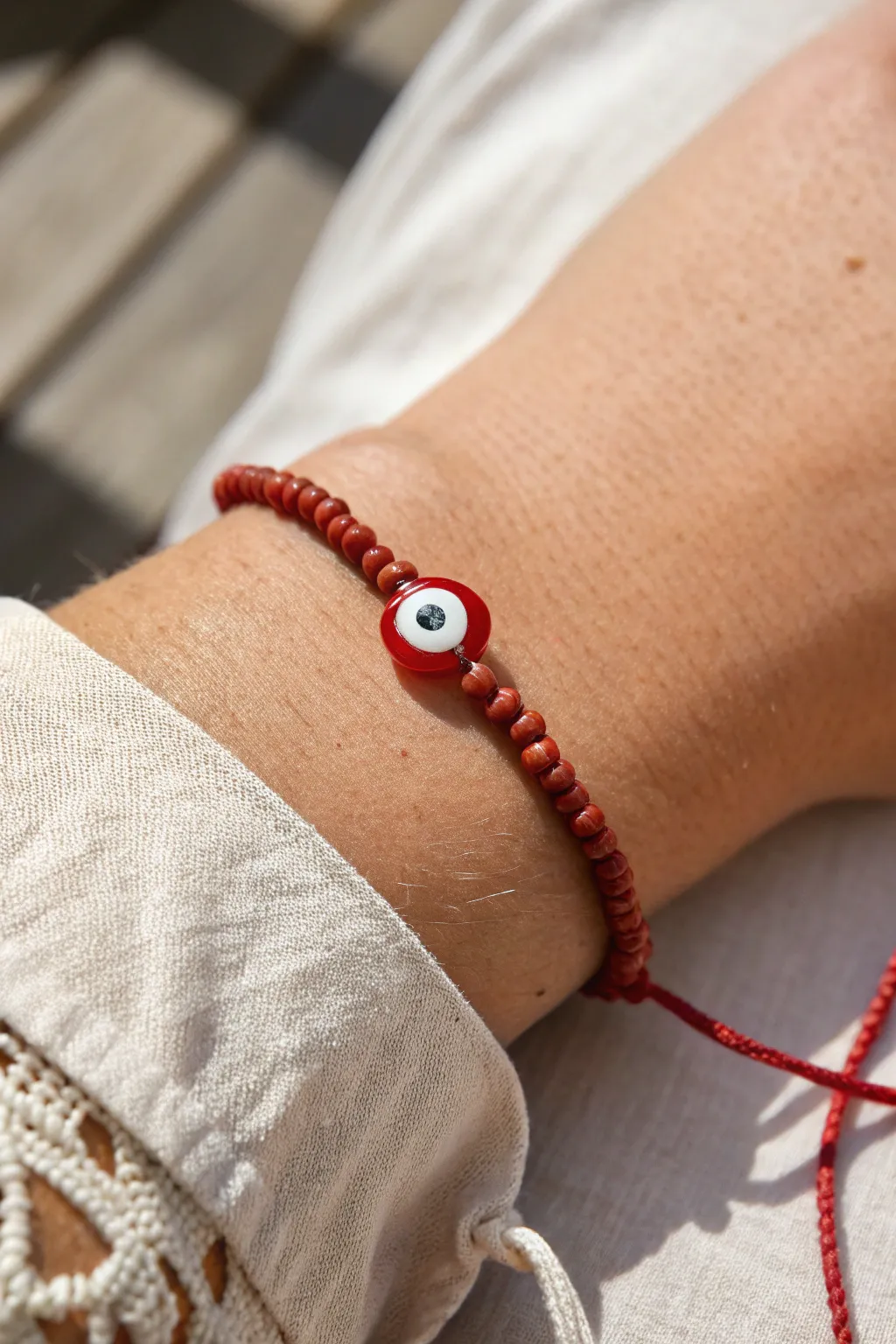 Minimal red clay bracelet with a red-toned evil eye bead, styled on wrist in soft daylight