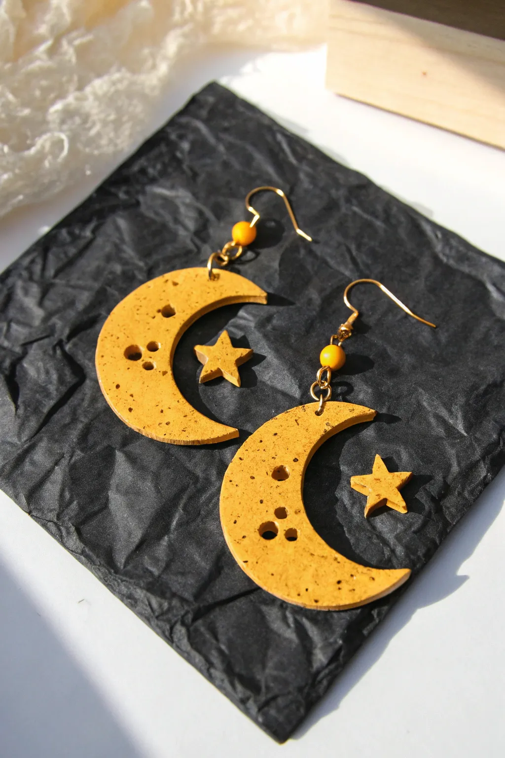 Bright yellow crescent moon clay earrings with star cutouts on dark paper for striking contrast.
